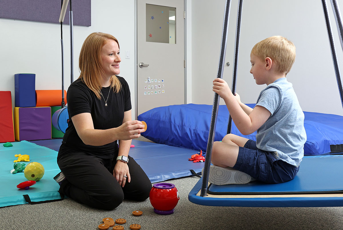 A child sits on a swing while working on literacy and counting skills with a speech therapist.